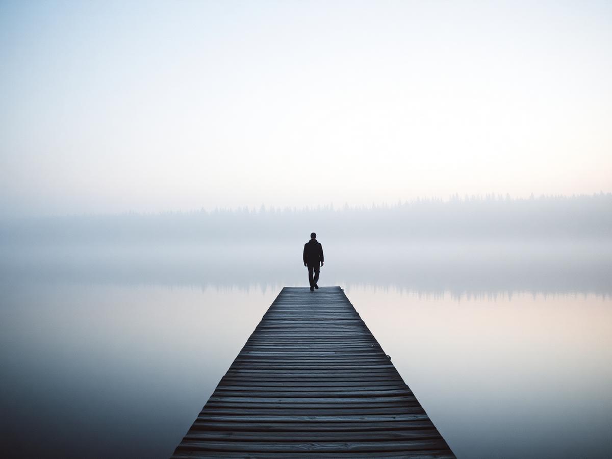 A figure walking on a pier over a misty Finnish lake at dawn.